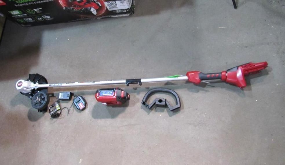 Red and silver string trimmer, with battery, charger, and guard on a concrete surface.