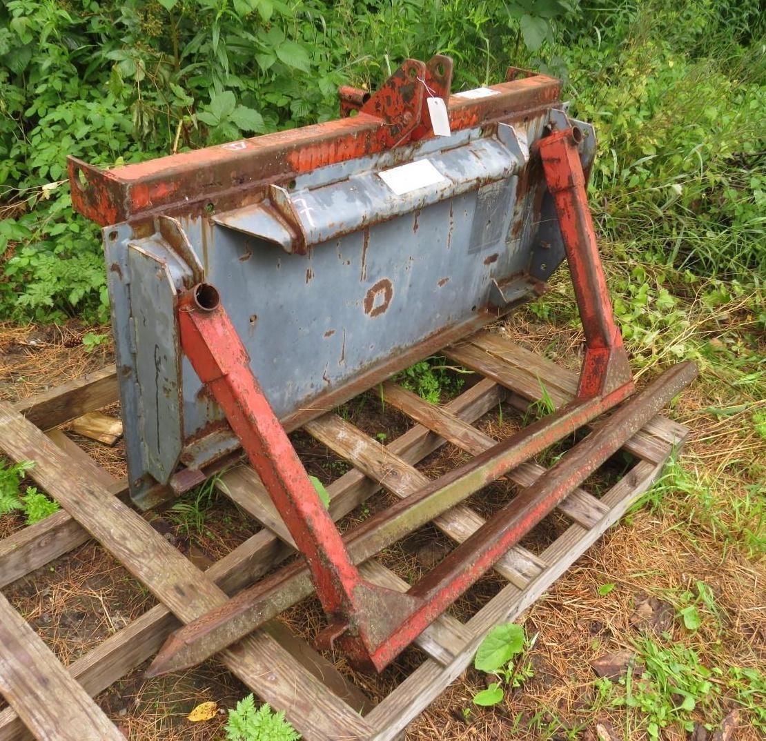 Gray and red metal tractor attachment on a wooden pallet, outdoors.