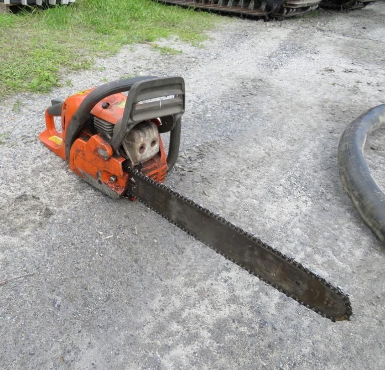 Orange chainsaw lying on gray gravel, blade extended.