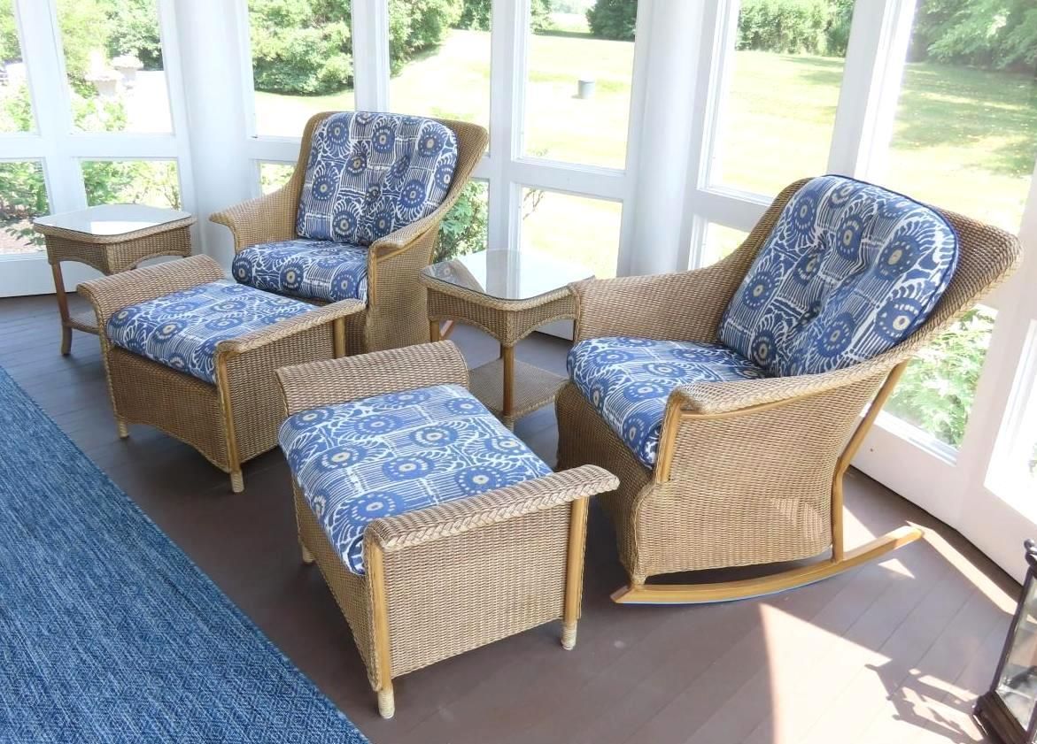 Wicker chairs with blue patterned cushions on a sun porch, two chairs with footrests.