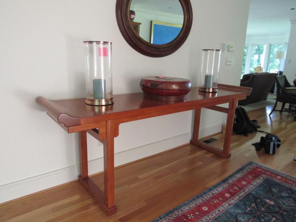 A wooden console table with decorations stands against a white wall below a round mirror.