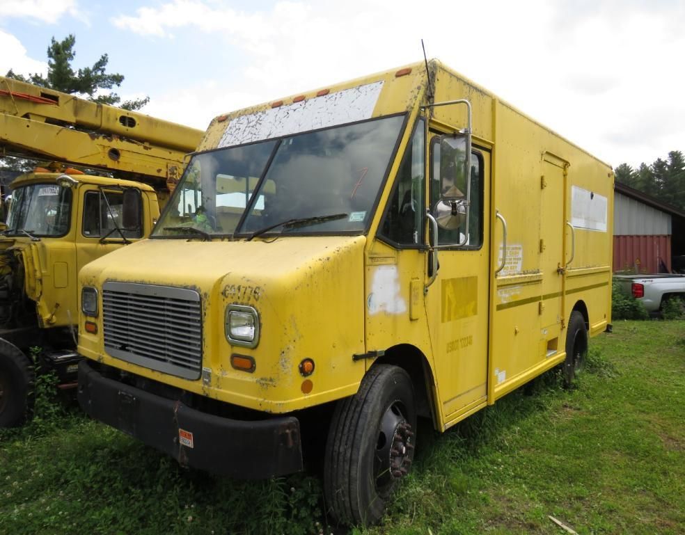 Yellow commercial box truck parked in a grassy area with other equipment.