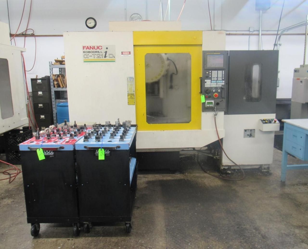 CNC milling machine in a workshop, with tool storage carts in front.