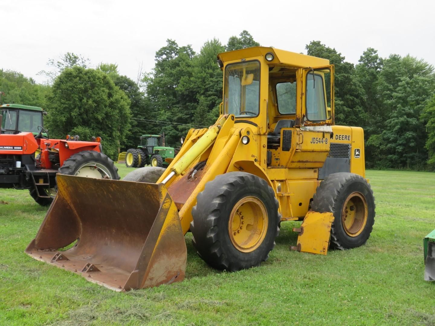Yellow front-end loader on grass; other farm equipment visible in the background.