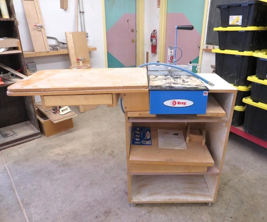 Woodworking table with scroll saw, drawers, and storage shelves.