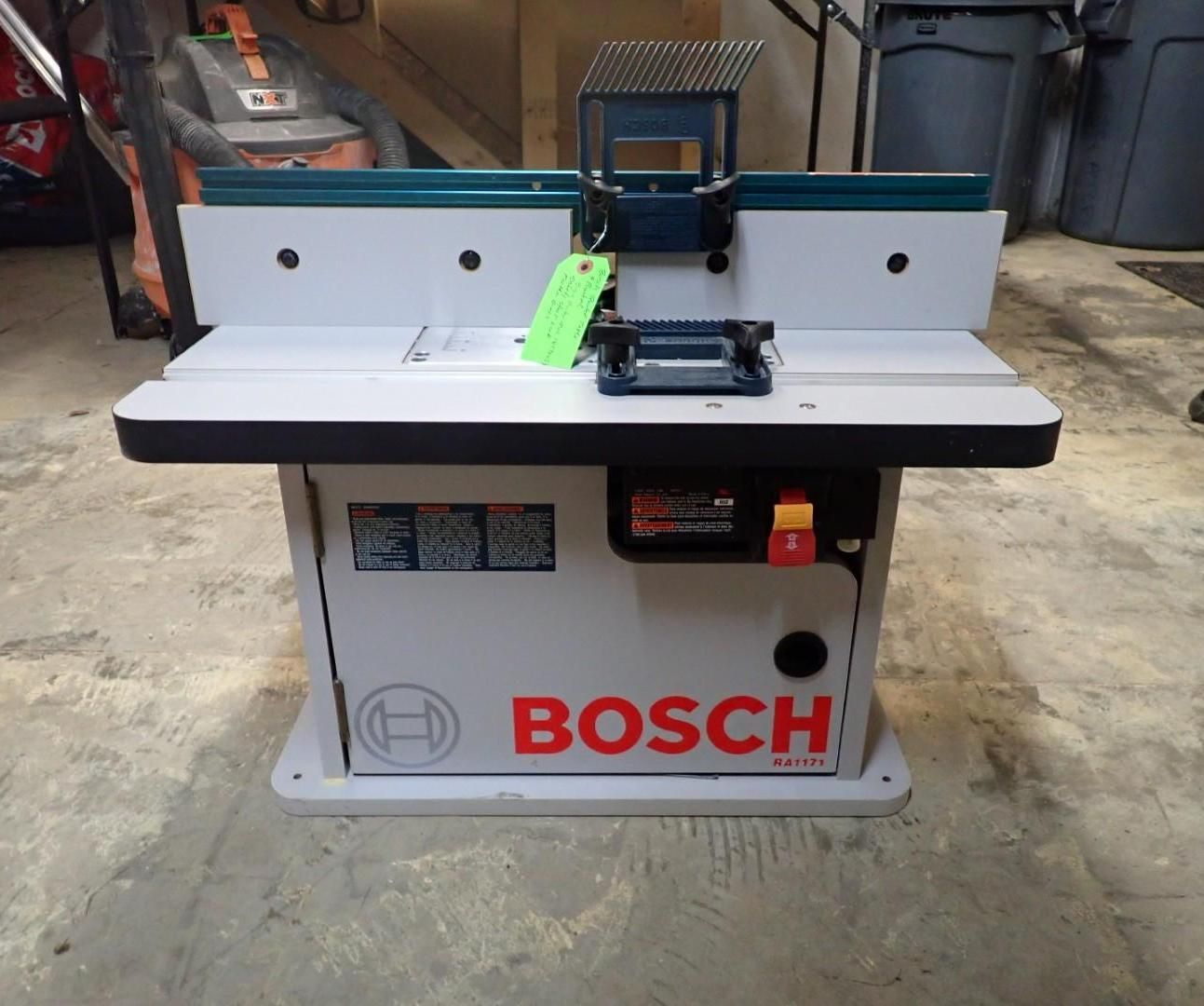 Bosch router table, white and teal, with a router mounted, power switch, and dust collection port.