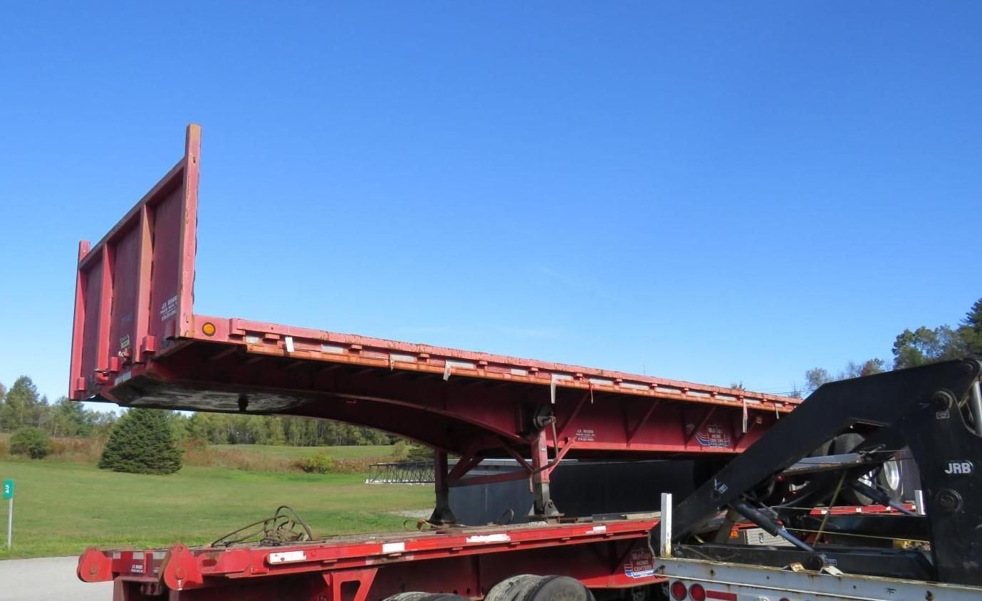 Red flatbed trailer with a raised front against a blue sky.