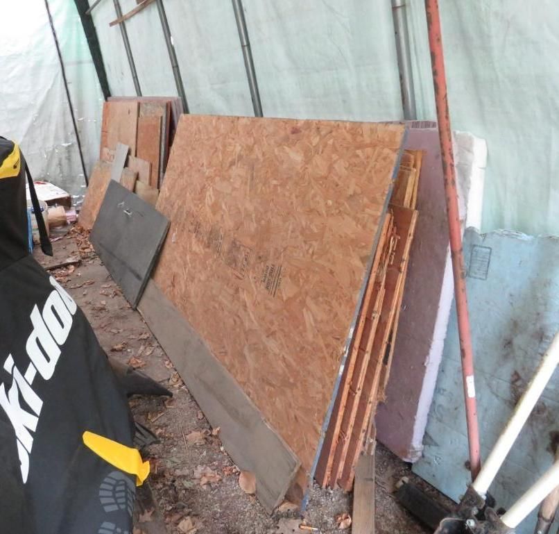 Pile of wood and building materials against a light green tarp in an outdoor area.