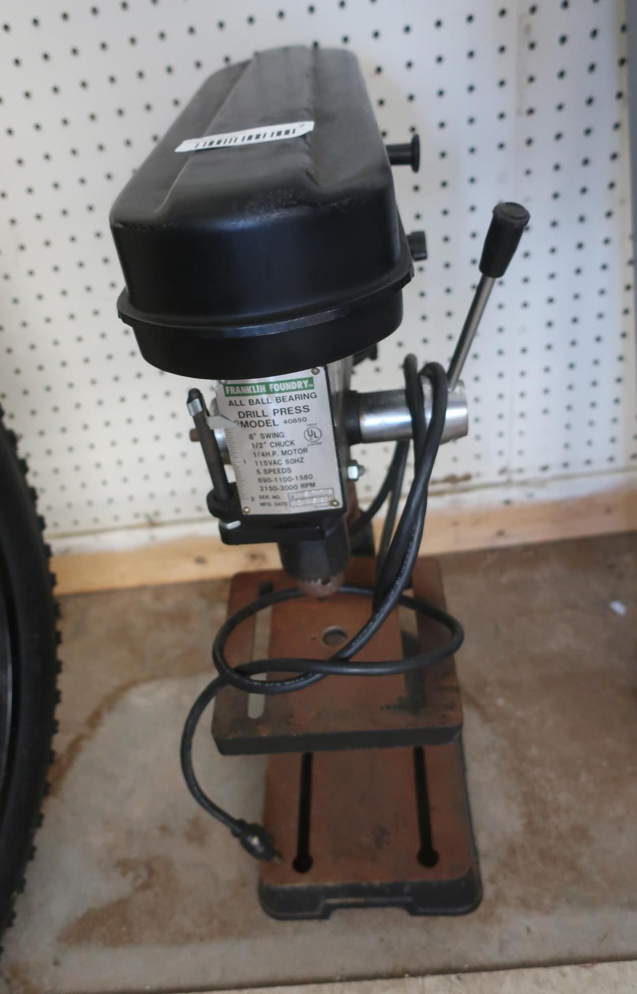 Black drill press on a brown metal stand with a black cord.