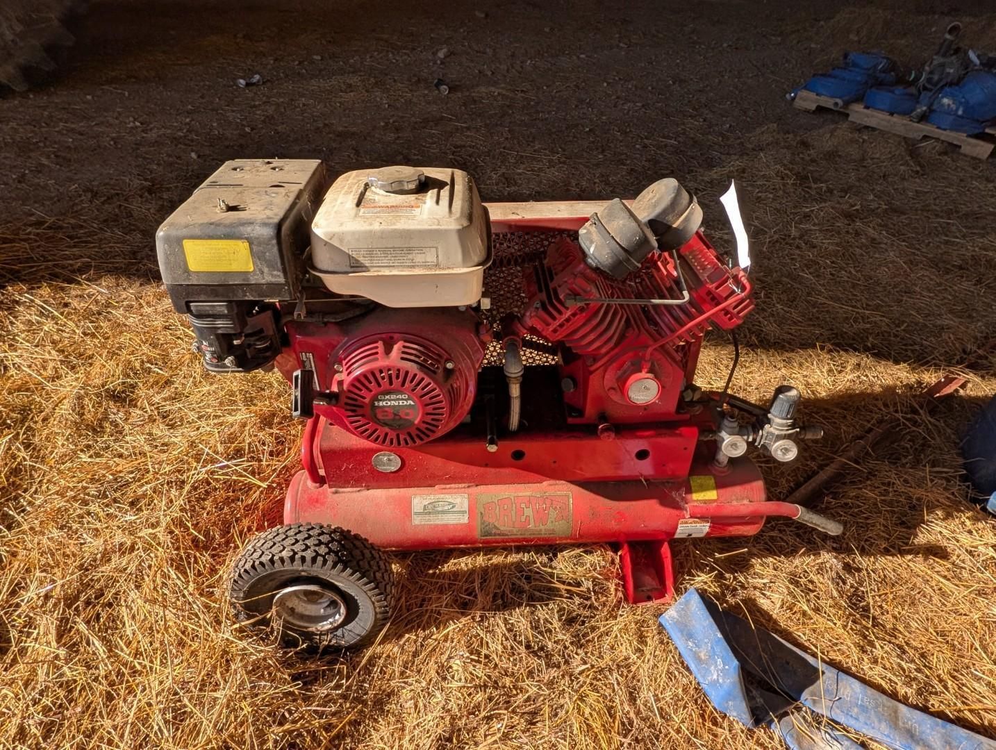 Red portable air compressor with engine and wheels on a straw-covered ground indoors
