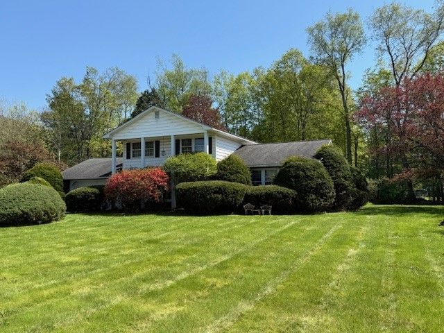 White house with large lawn and manicured bushes under a blue sky.