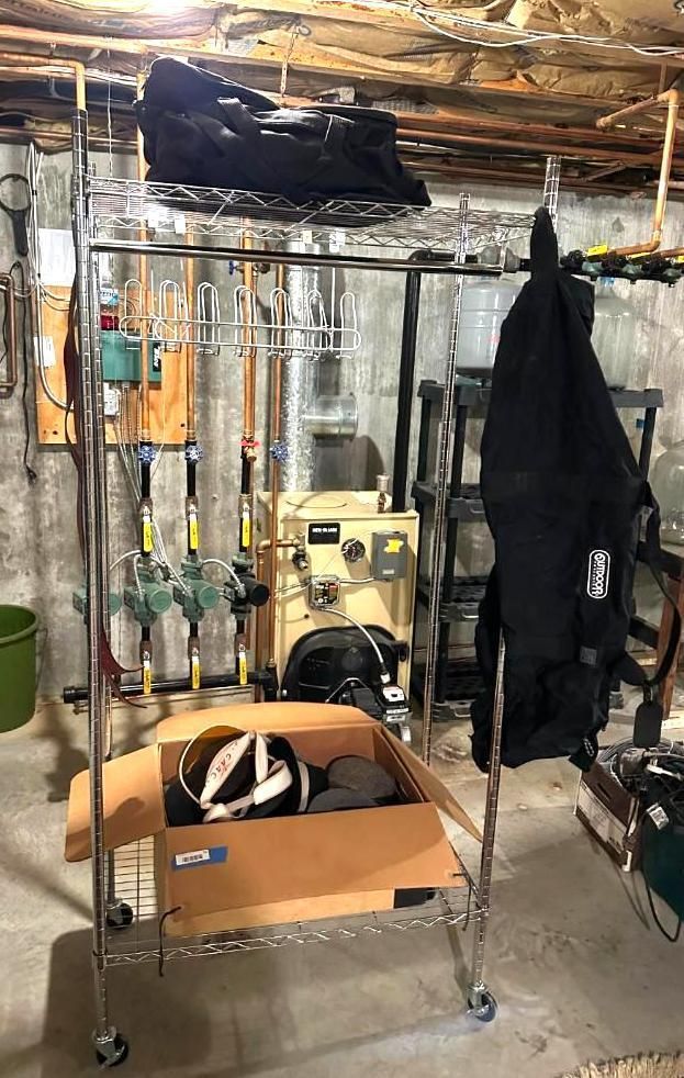 Metal shelving unit in a basement, holding boots, clothing, and a cardboard box.