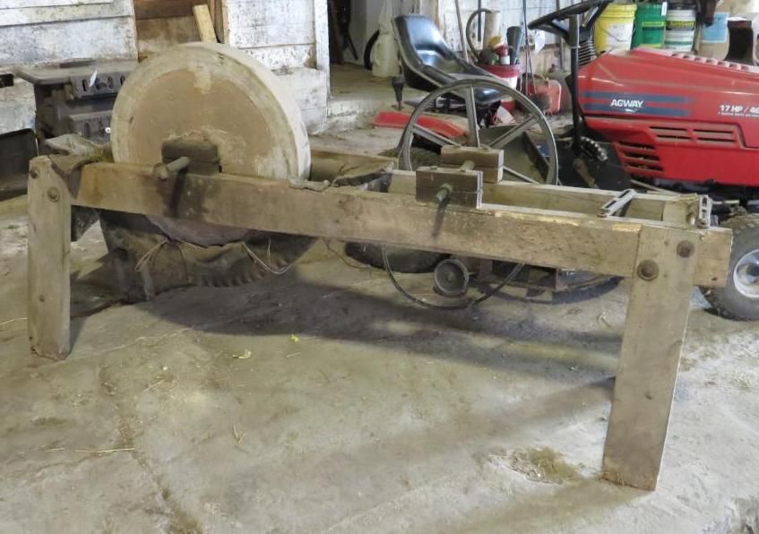 Stone grinding wheel on a wooden frame, in a garage with a red riding mower.