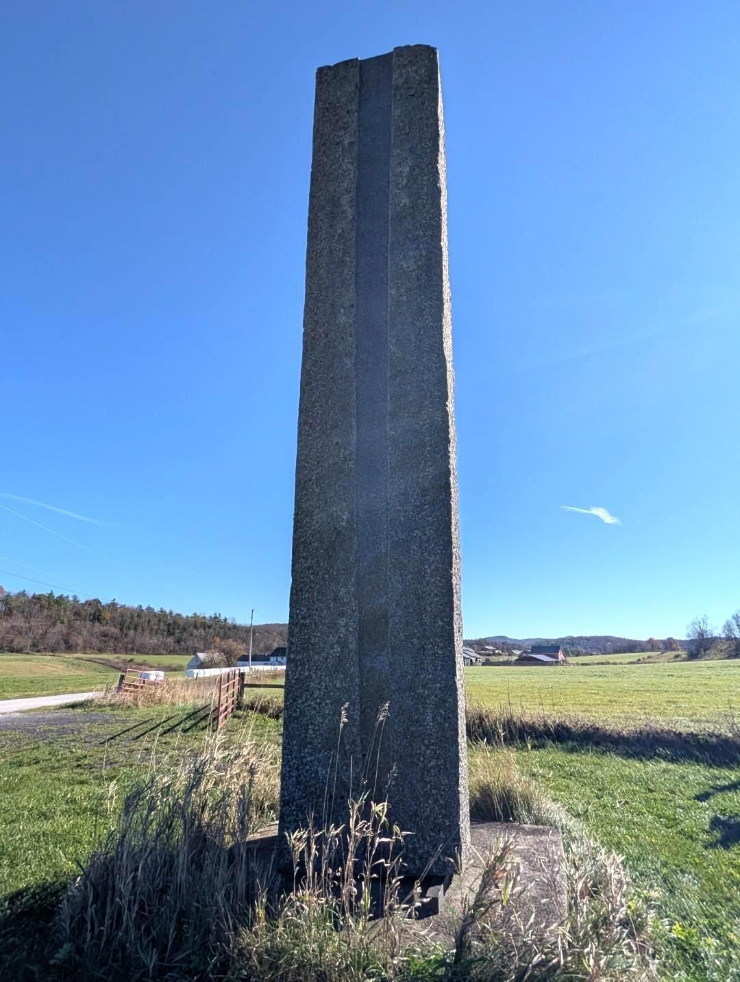 Tall dark stone monolith standing in a grassy field under a clear blue sky