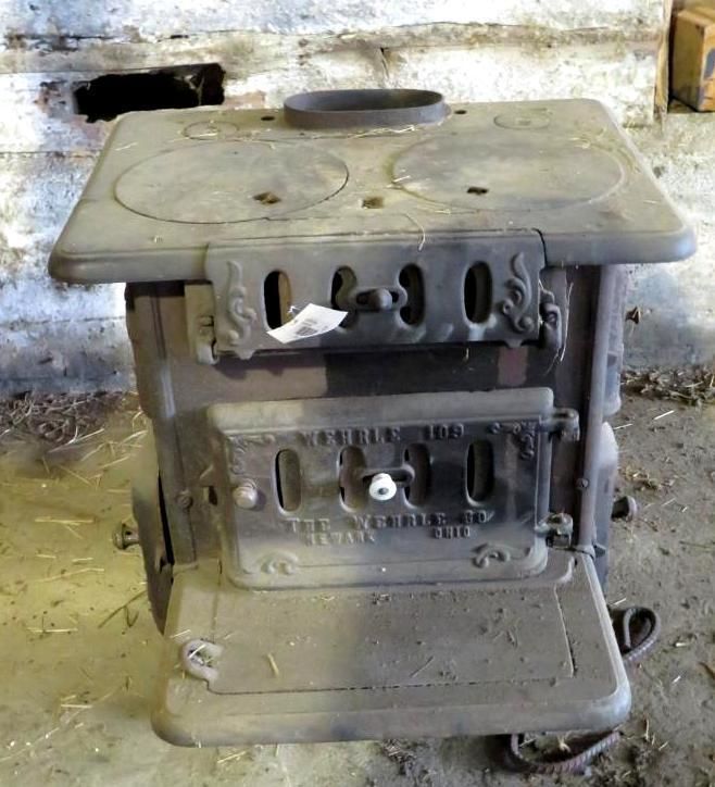 Antique wood-burning stove, gray cast iron with two burner covers and an oval chimney, indoors in a barn.