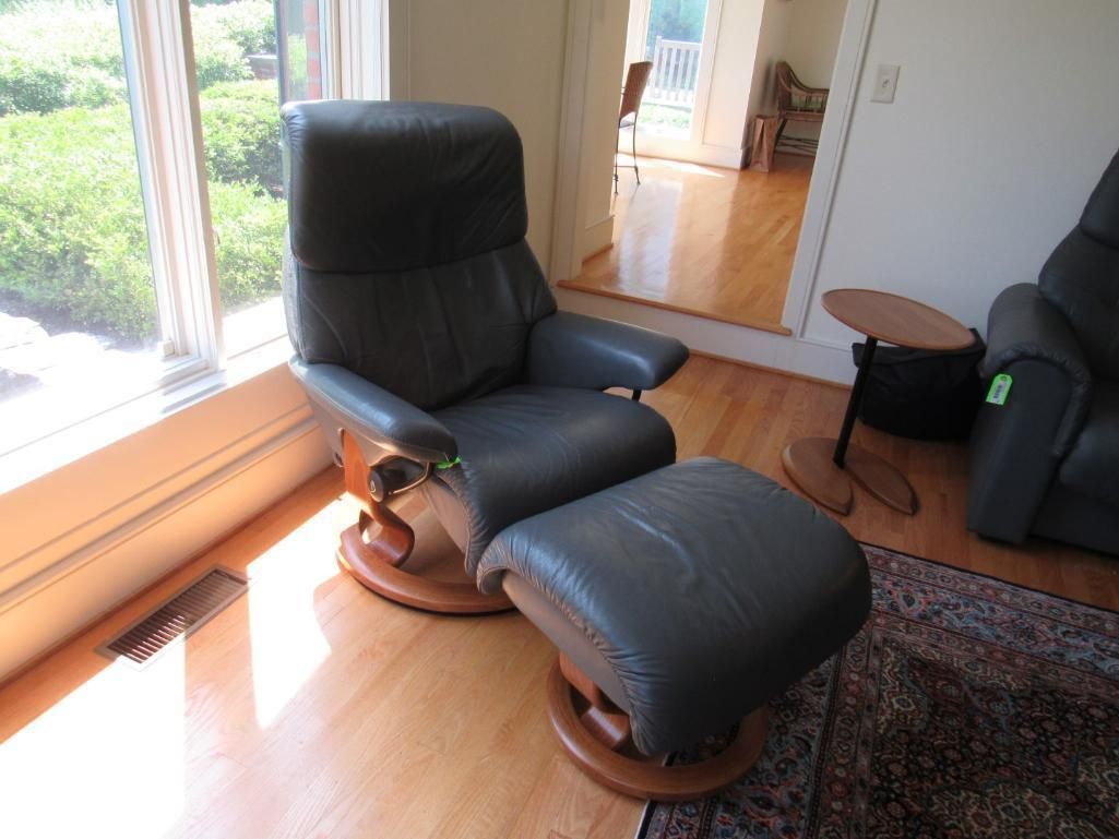 A dark blue leather recliner chair and ottoman on a wooden base near a window.