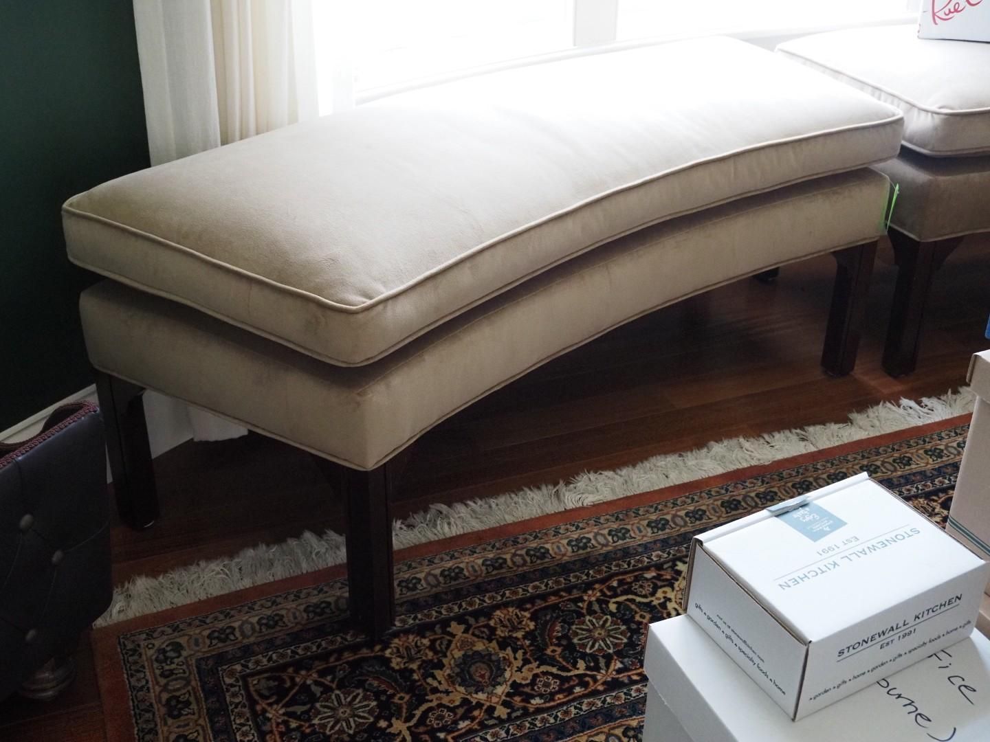 Beige upholstered bench with curved seat, dark wooden legs, and off-white piping.