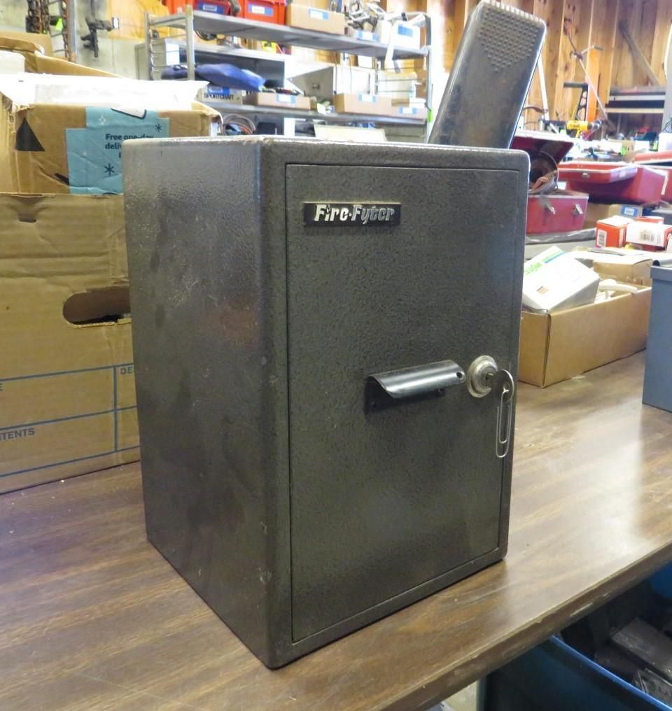 Dark gray Fire-Fighter safe on a wooden table. Key in the lock, handle extended.