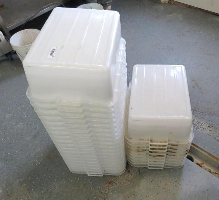Stacks of white, lidded plastic storage containers on a concrete floor. One stack is taller than the other.