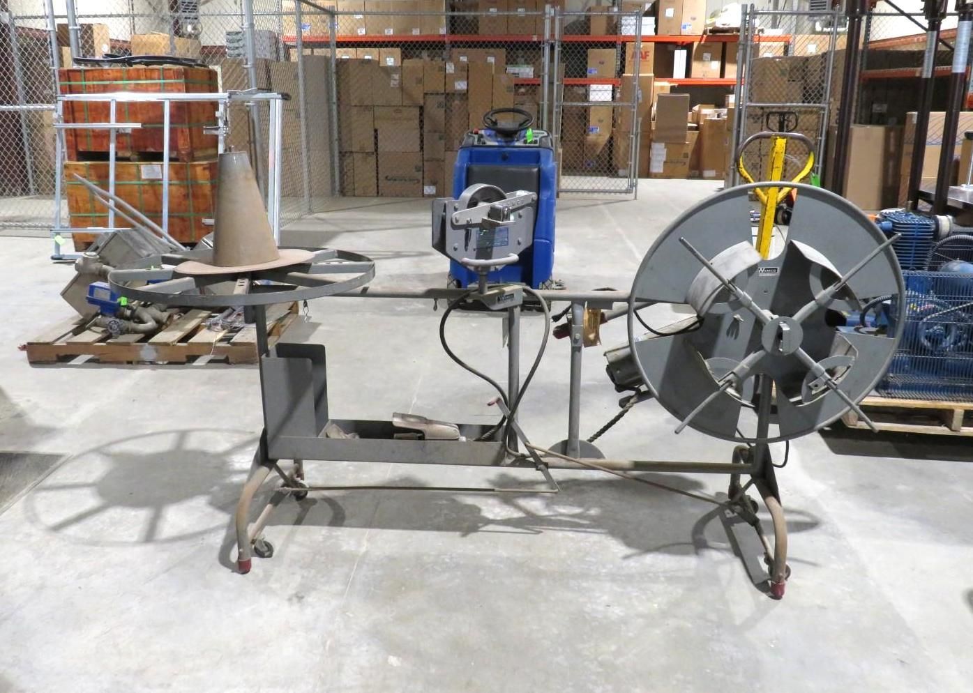 A large metal wire spooling machine in a warehouse setting, with a cone-shaped guide and a blue motor.