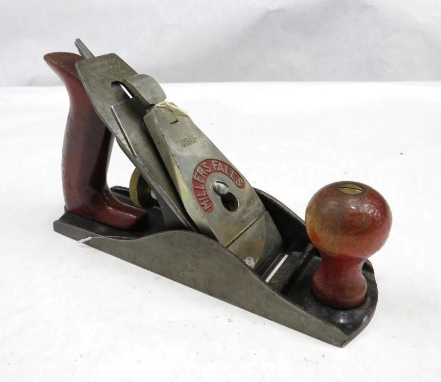 Hand plane with red wooden handles and a metal blade, lying on a white surface.