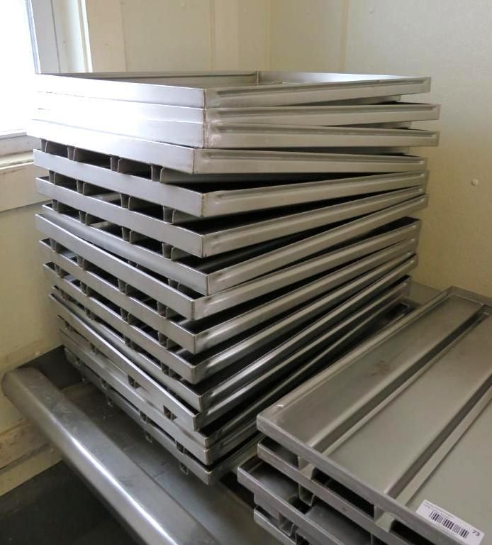 Stack of rectangular stainless steel trays on a stainless steel surface, near a window.