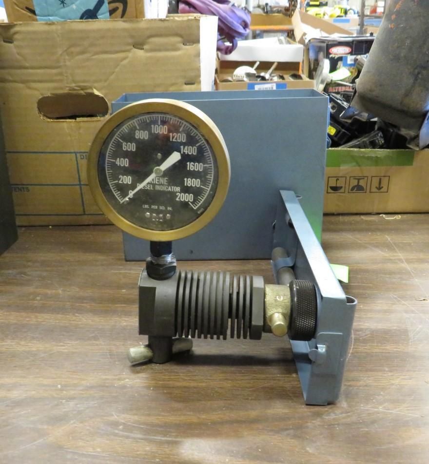 Pressure gauge with brass dial, mounted on a blue metal bracket. Gauge reads up to 2000.