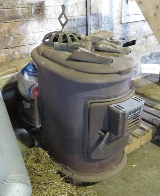 Metal stove in a barn, with a door, decorative top, and vent.