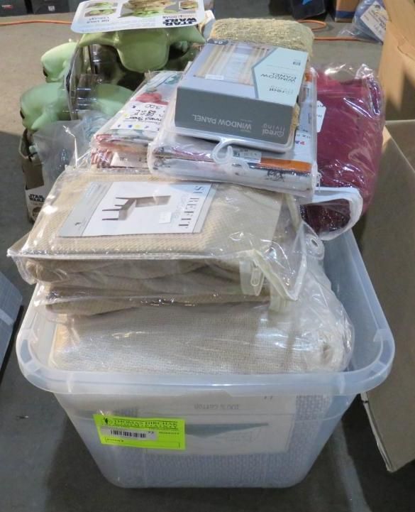 Clear plastic bin overflowing with folded fabric items, including curtains and tablecloths.