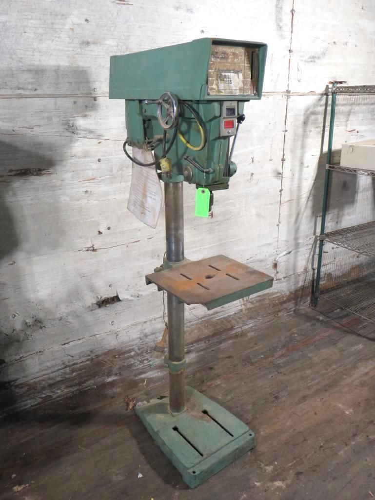 Green drill press in a workshop setting.
