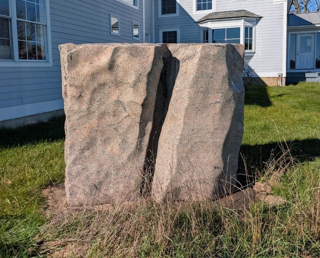 Large split boulder on grass beside a white house in daylight