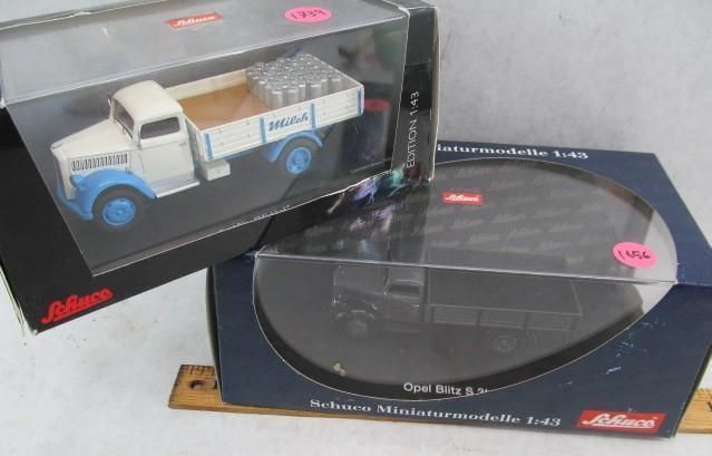 Two model trucks in boxes, one blue and white, the other gray, side by side.