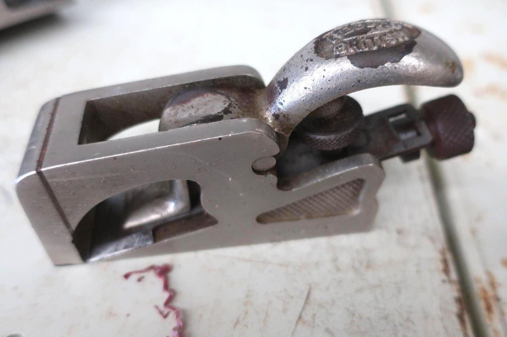 A small metal tool, likely a plane, sits on a surface. It has a handle, blade adjustment.