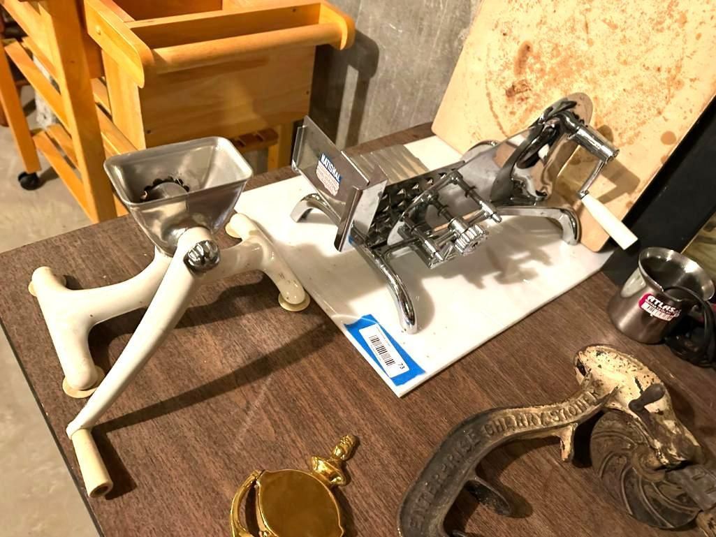 Two vintage meat grinders on a surface, next to a wooden cart and other items.