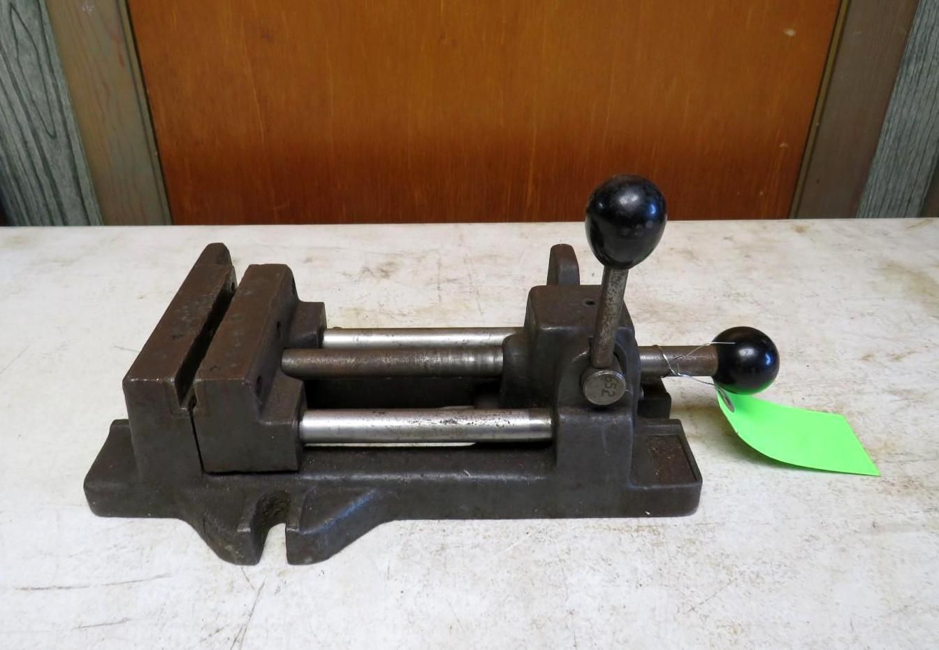 Metal vise with black handles, clamping mechanism, and attached green tag.