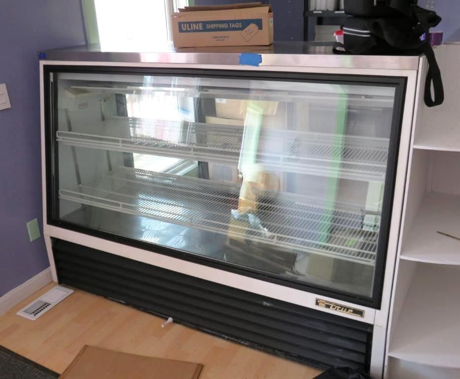 Commercial refrigerated display case, stainless steel trim, glass front, shelves, indoors.