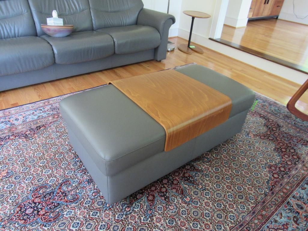 Gray ottoman with a wooden tray, in front of a gray couch on a patterned rug.