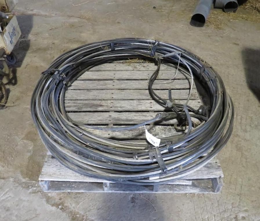 Coiled black cables, bound with ties, rest on a wooden pallet indoors.