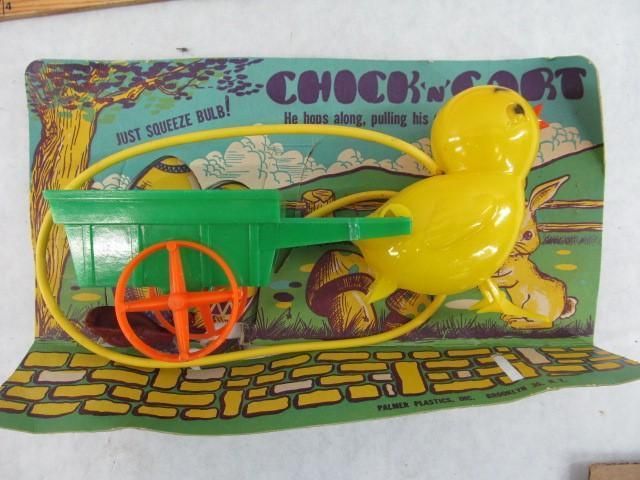 Yellow chick toy pulling a green wheelbarrow on a cardboard backing with a rabbit scene.