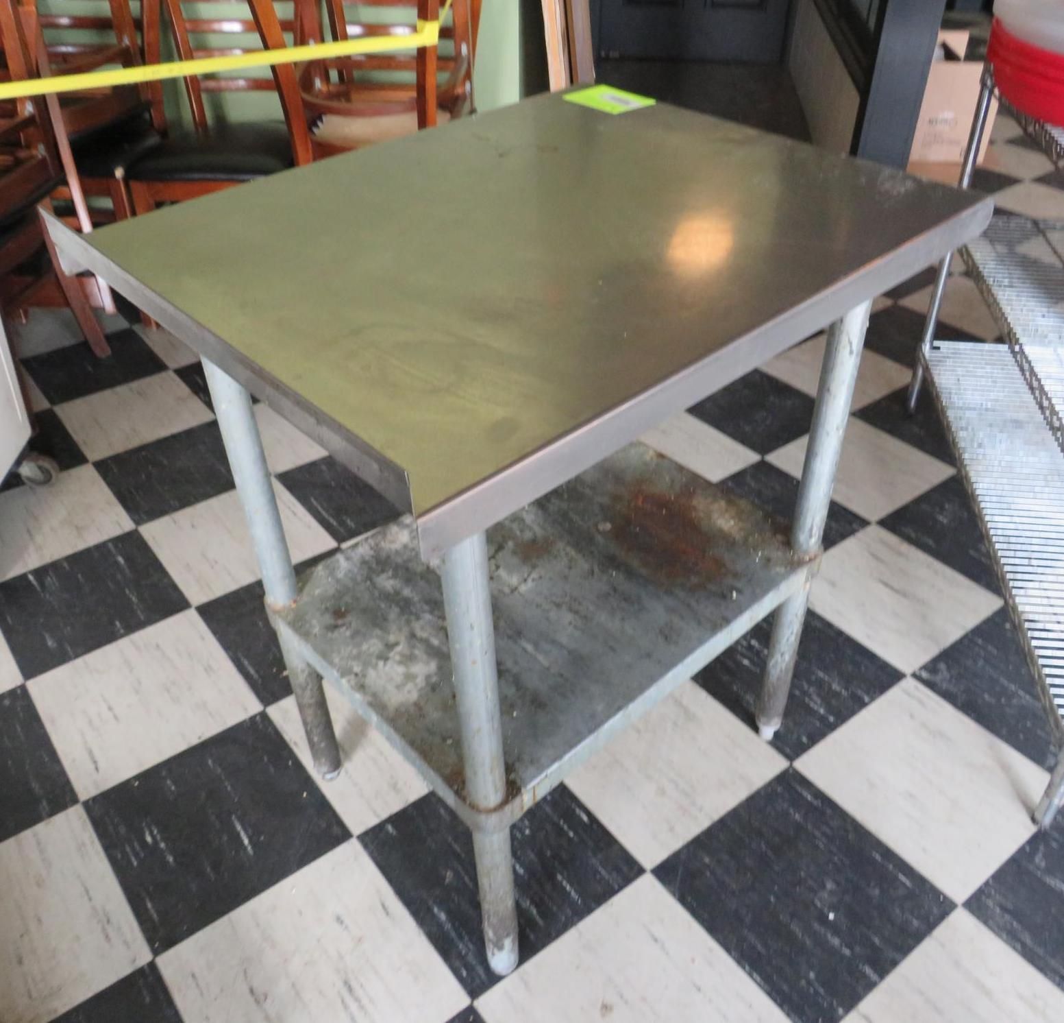 Stainless steel kitchen work table on a black and white checkered floor, with a lower shelf.