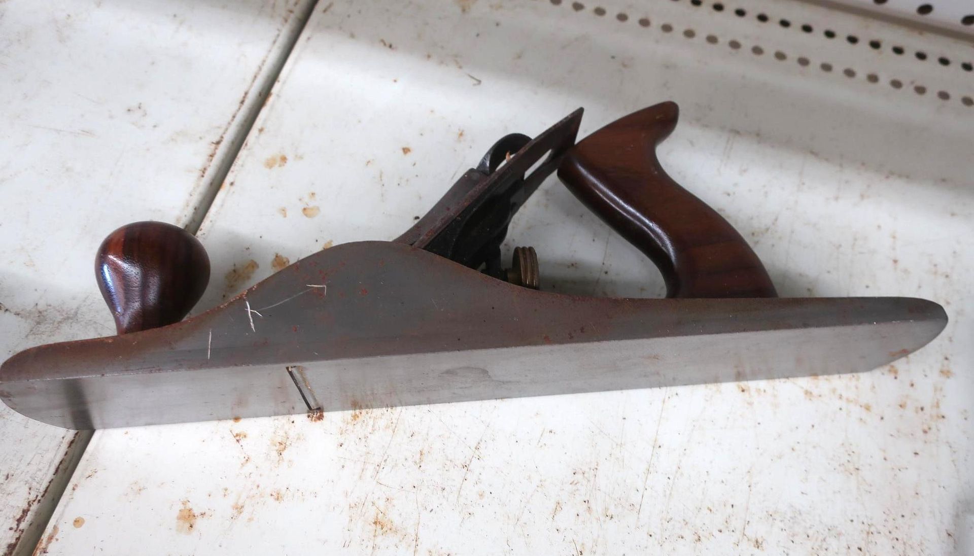 A brown and metal hand plane with a wooden handle and knob on a white surface.