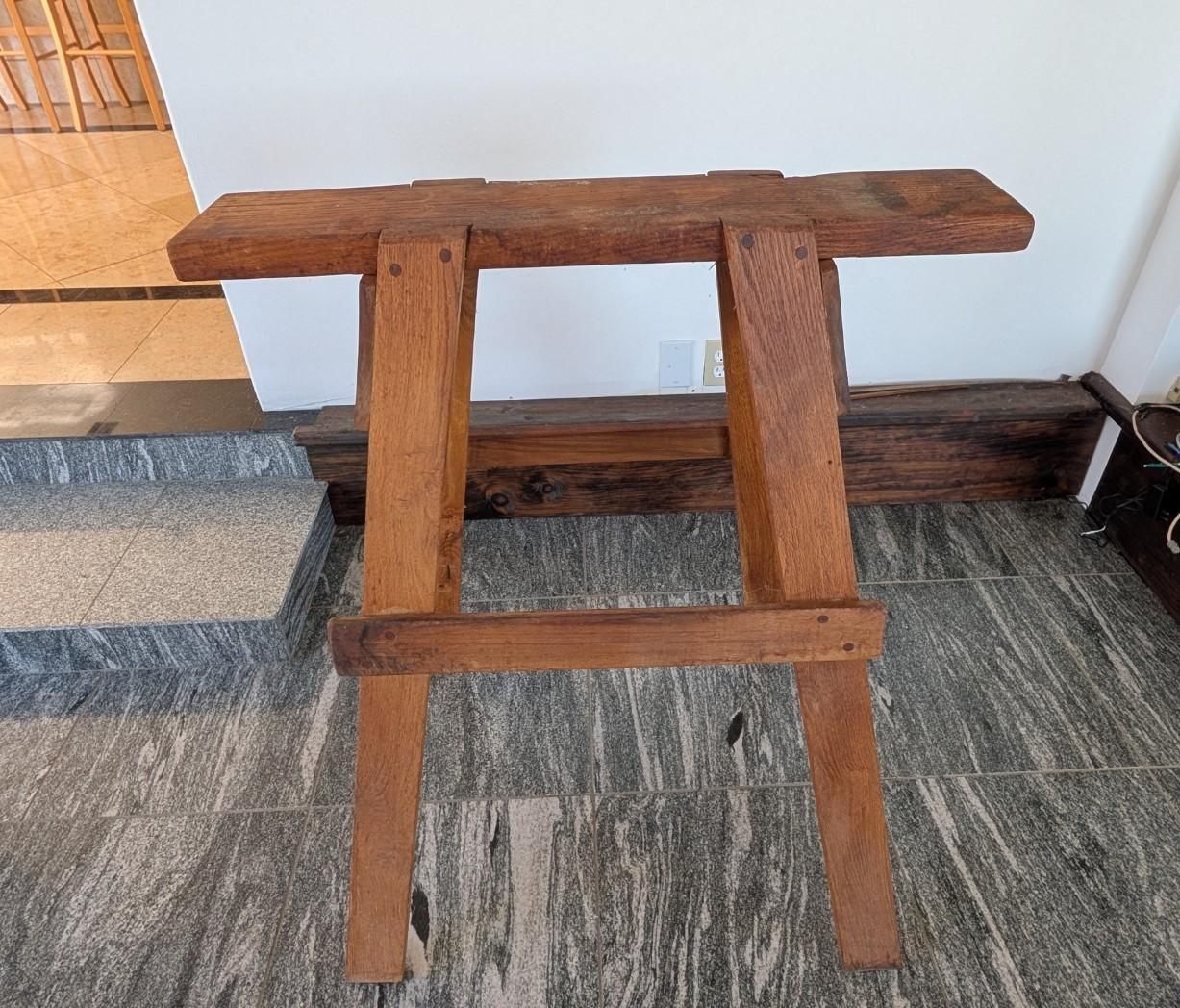 Wooden folding table or stand with a cross-braced frame against a light wall indoors