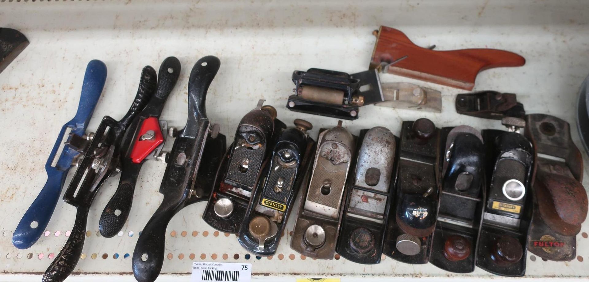 Collection of hand planes of various shapes and sizes on a shelf. Includes a blue spoke shave and red handled tool.