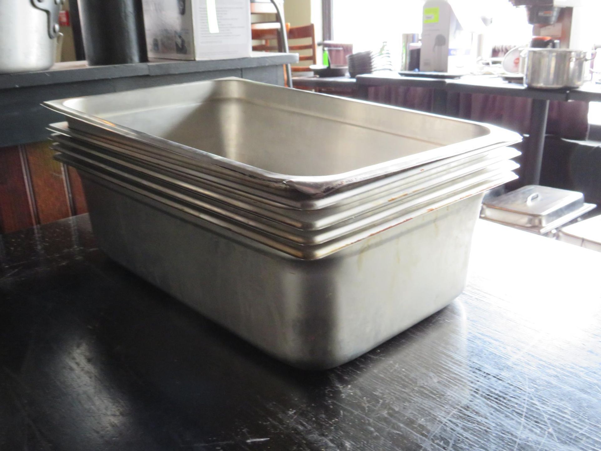 Stack of stainless steel food storage pans on a dark tabletop, likely in a commercial kitchen.
