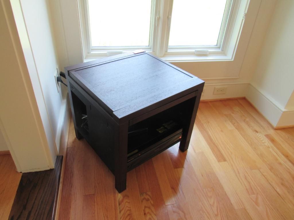 Dark brown side table in corner of room with a window.