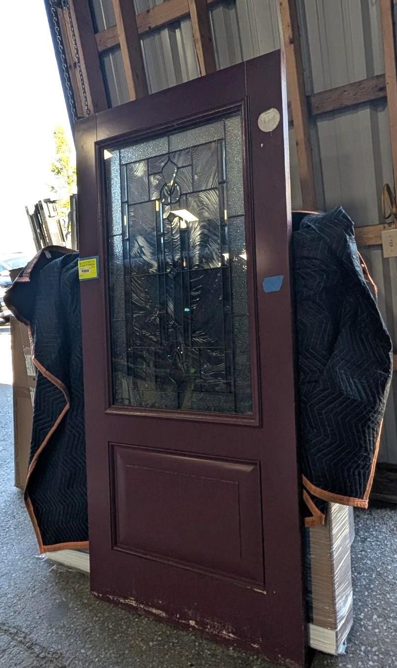 Dark brown front door with glass panel leaning against a wall, flanked by two wrapped items.