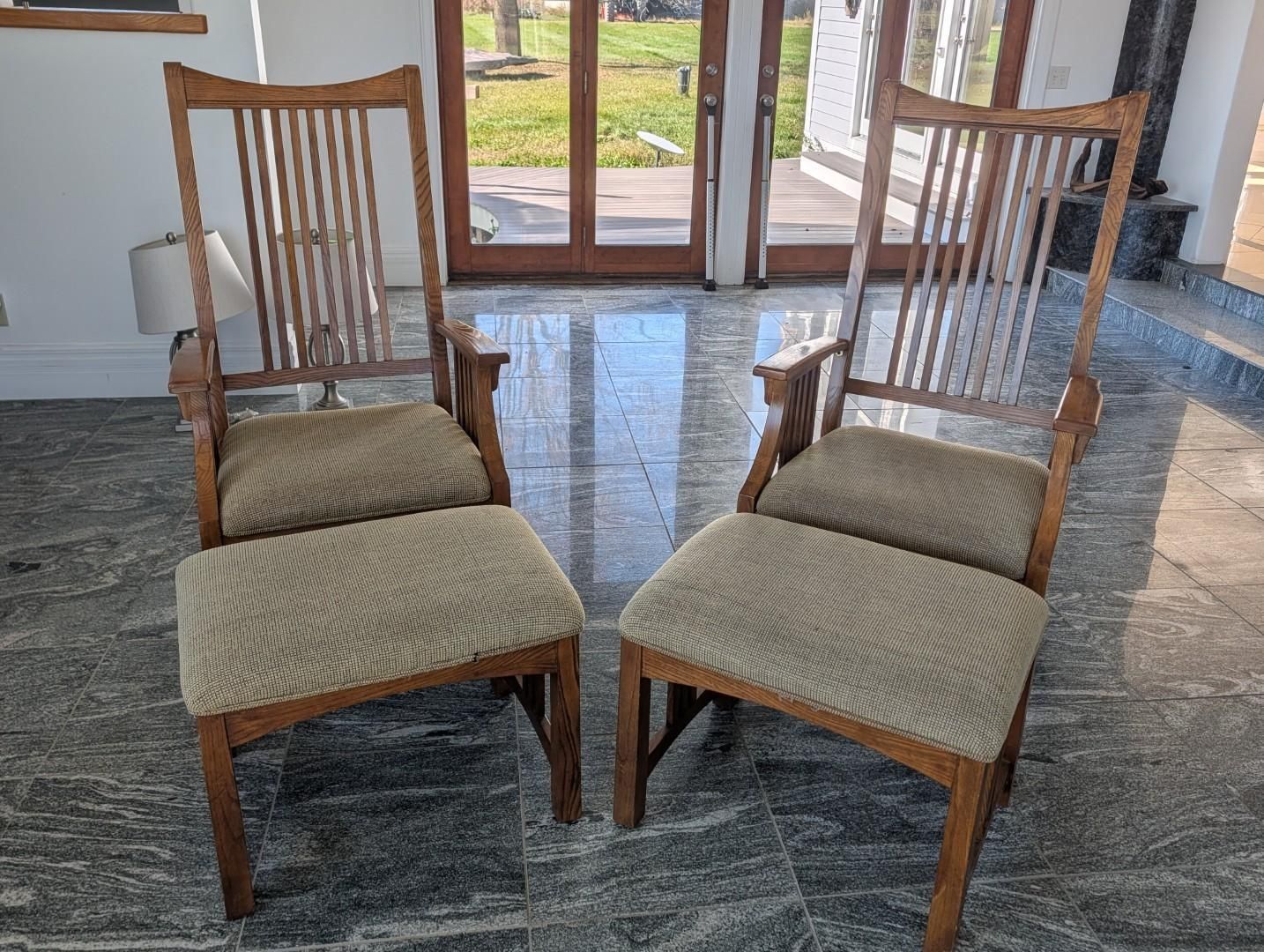 Two wooden chairs with beige cushions on a stone floor in a bright room by glass doors