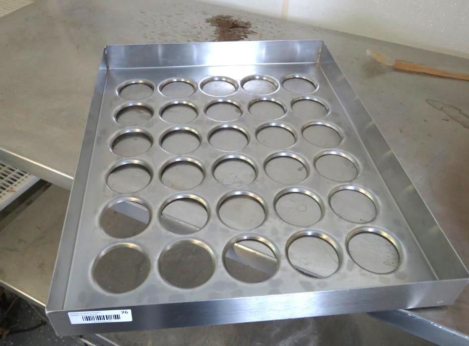 Stainless steel tray with circular cutouts on a metal surface.