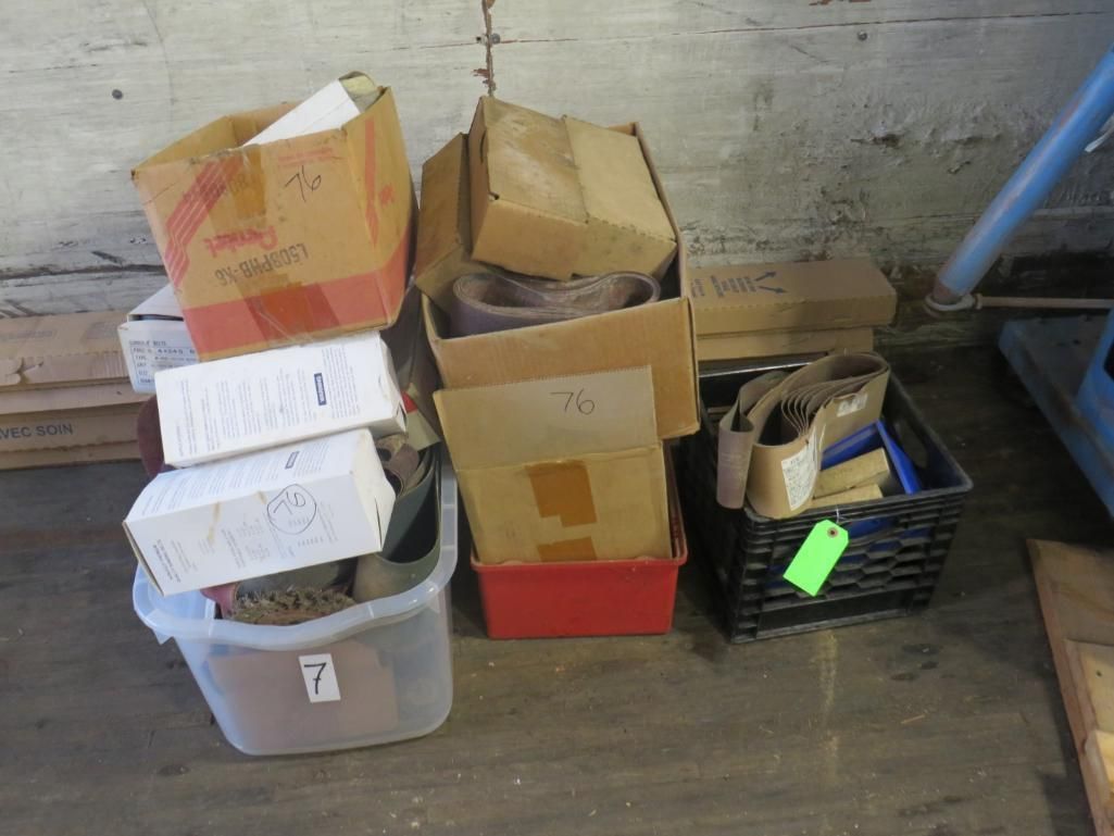 Boxes and bins filled with various items, possibly parts, sit on a concrete floor in a warehouse setting.