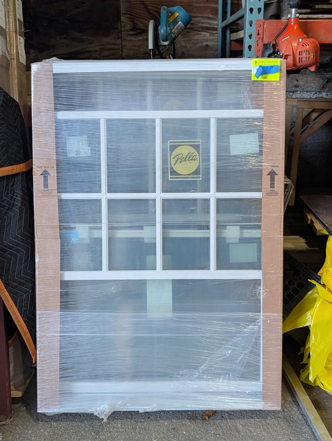 Wrapped white window frame with grid panes leaning in a storage area